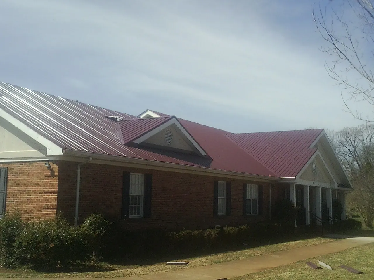 Red metal roof with gabled entries on a long brick building, from a Hail Damage Roof Repair job in Smithfield