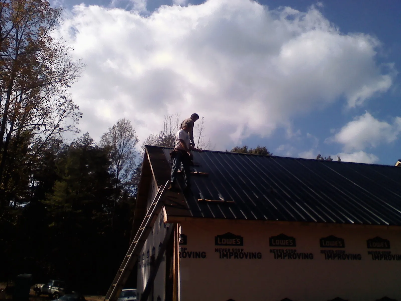 Roofer fastening dark metal panels high against a cloudy sky, from a Roof Inspection job in Smithfield