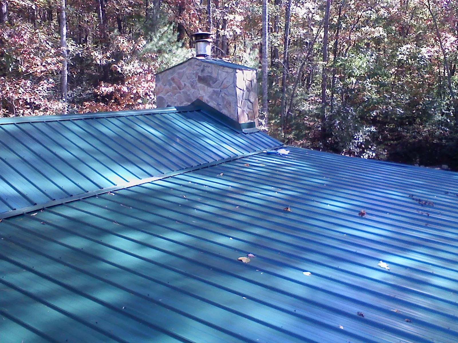 New green metal roof and stone chimney surrounded by autumn woods in Smithfield